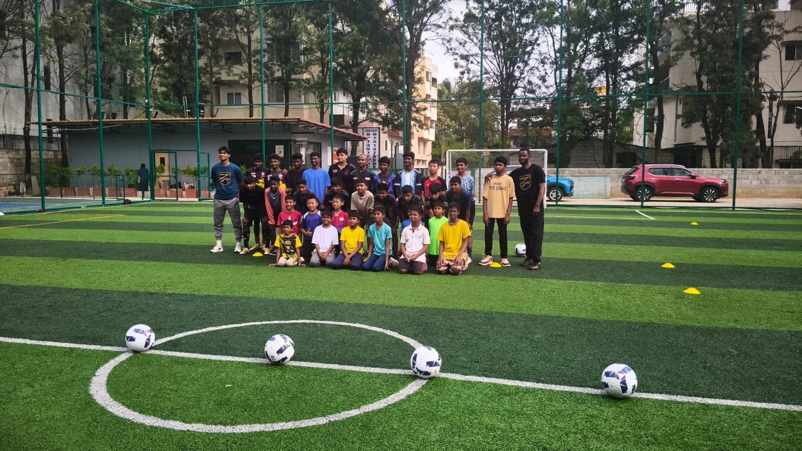 A group of children and two coaches gathered on a football pitch with match balls in the foreground.