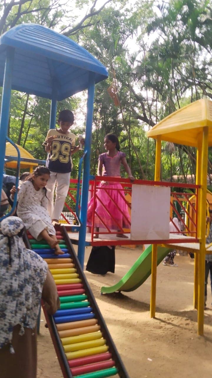 Children climbing a slide and play frame among trees.