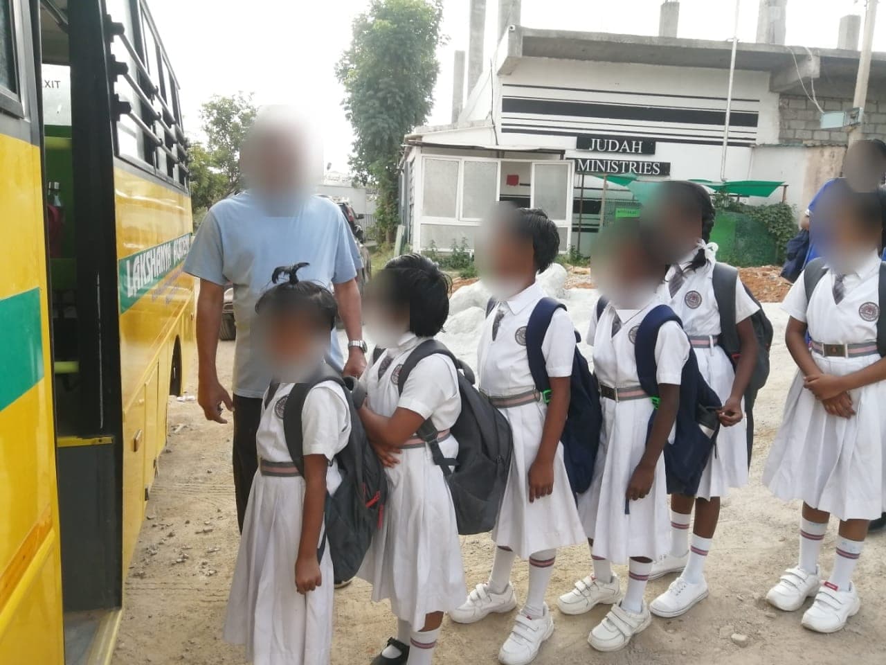 Children in school uniform with backpacks waiting to board a yellow bus. Faces are obscured to protect the children's privacy.