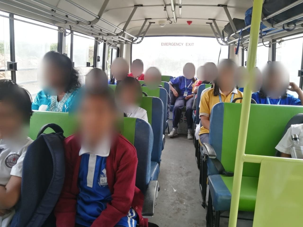 Children seated in the green and blue seats of a school bus with a staff member. Faces are obscured to protect the children's privacy.
