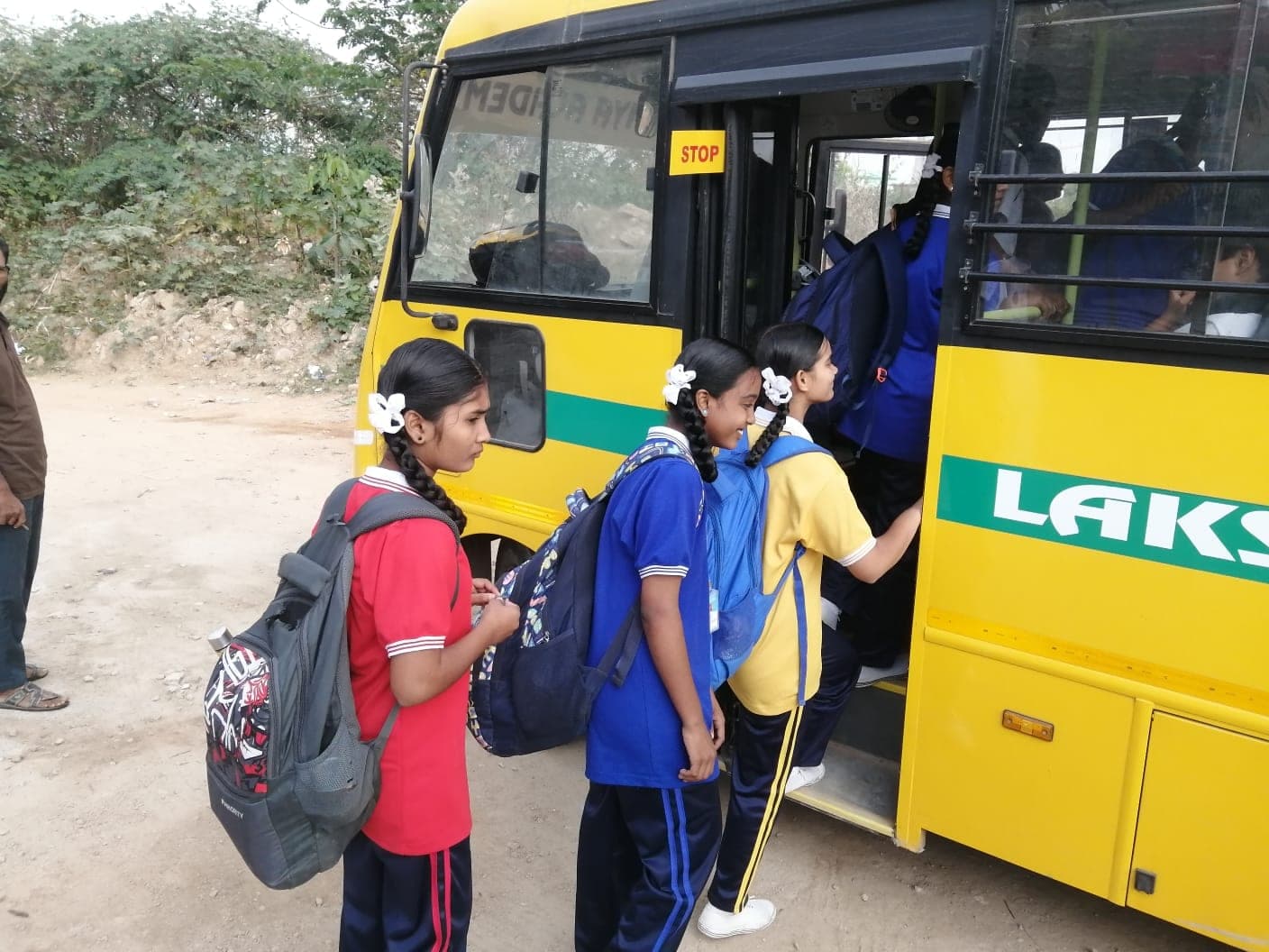 Children in school uniform with backpacks stepping onto a yellow school bus.