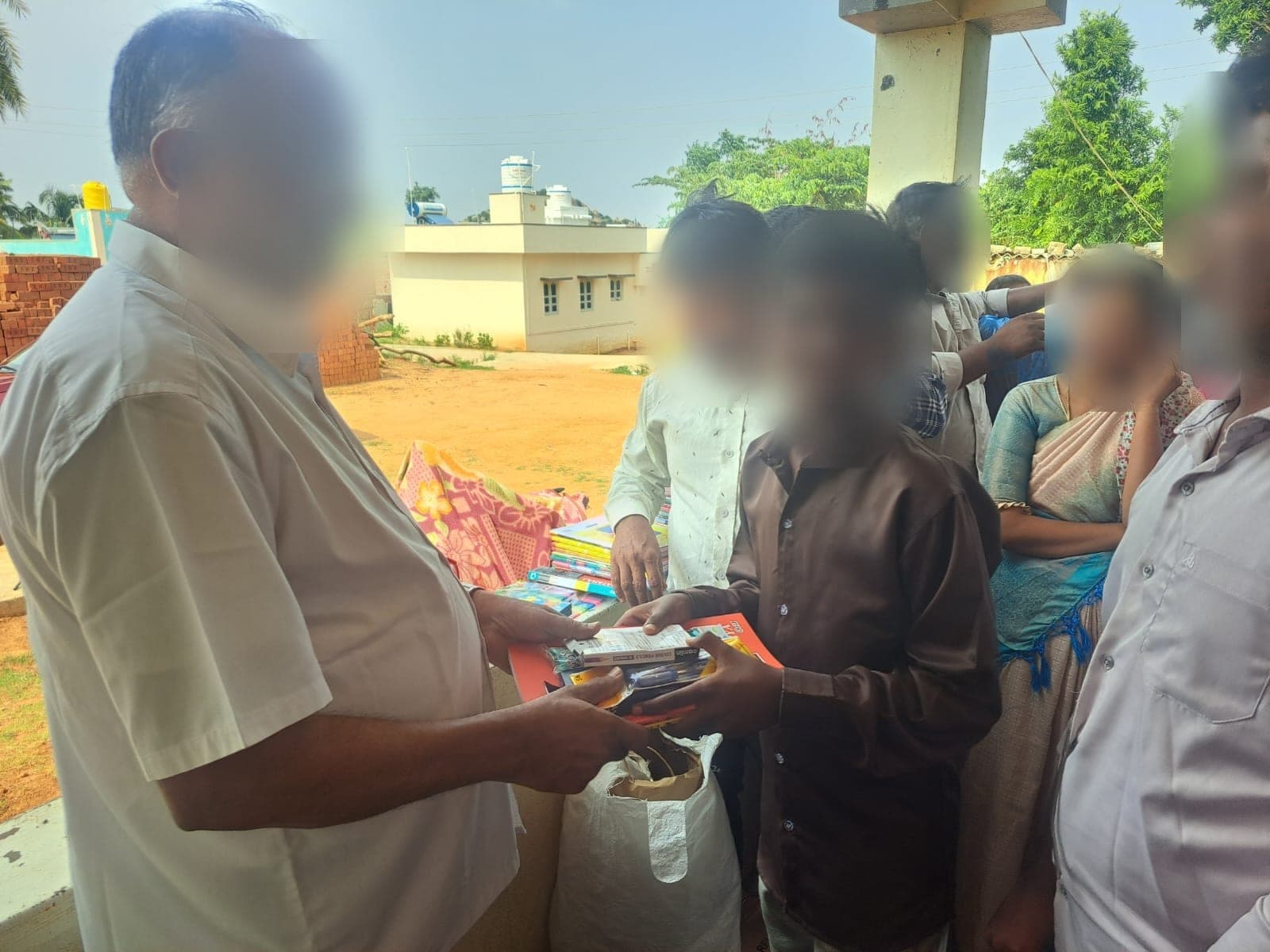 A boy accepting a bundle of stationery while villagers look on. Faces are obscured to protect the children's privacy.