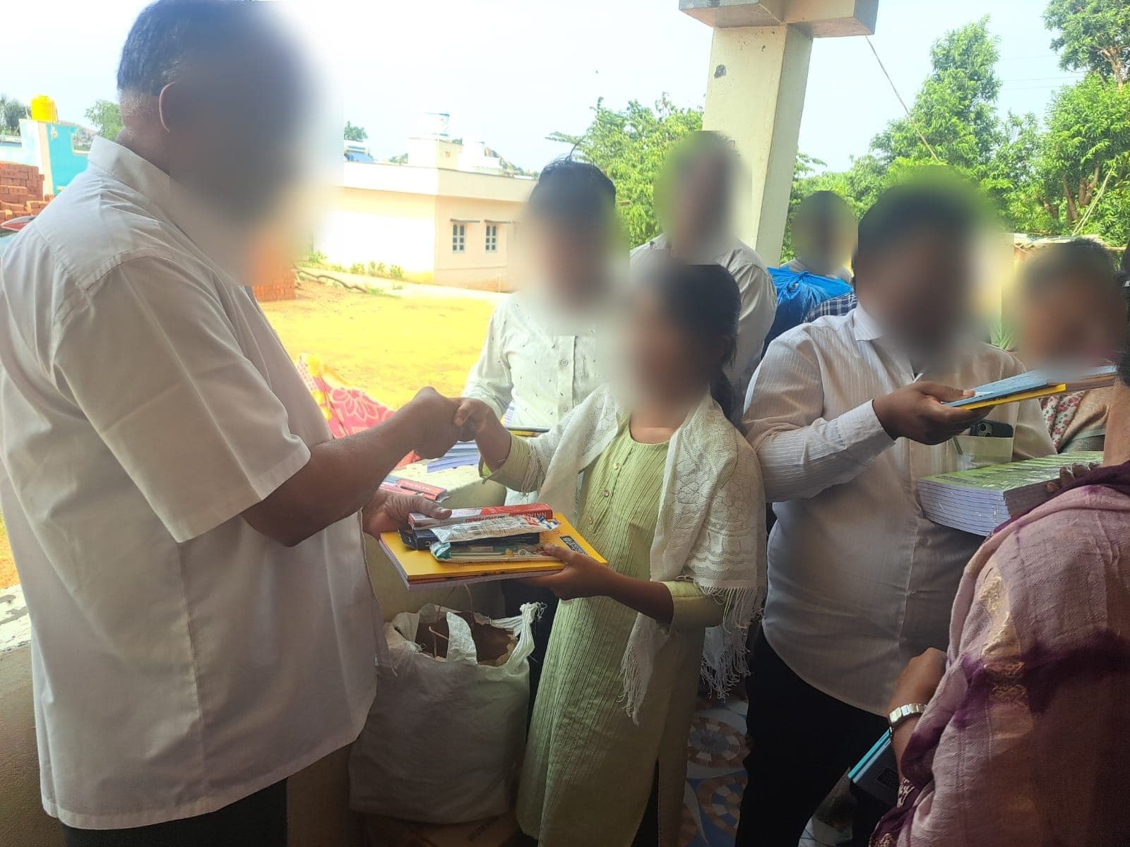 A student taking a stack of notebooks and a pen from the founder. Faces are obscured to protect the children's privacy.