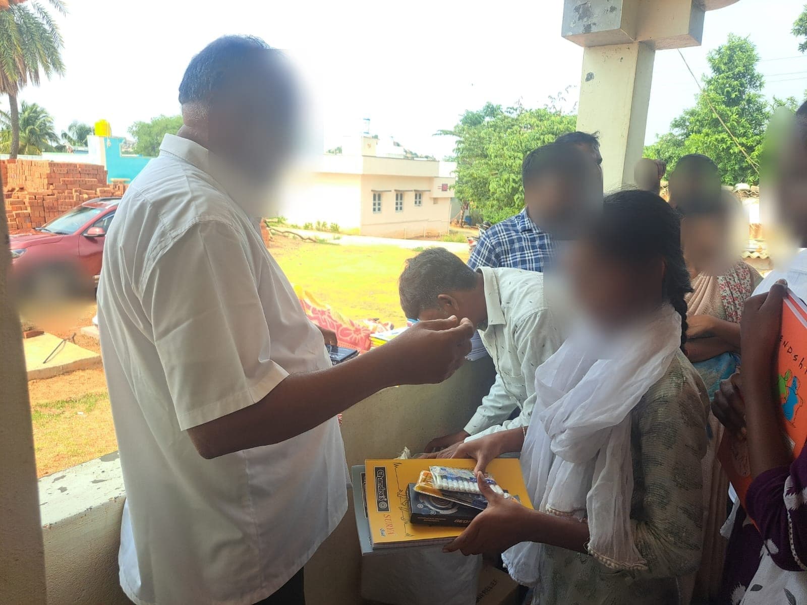 The founder offering a blessing to a student who is receiving a set of school supplies. Faces are obscured to protect the children's privacy.