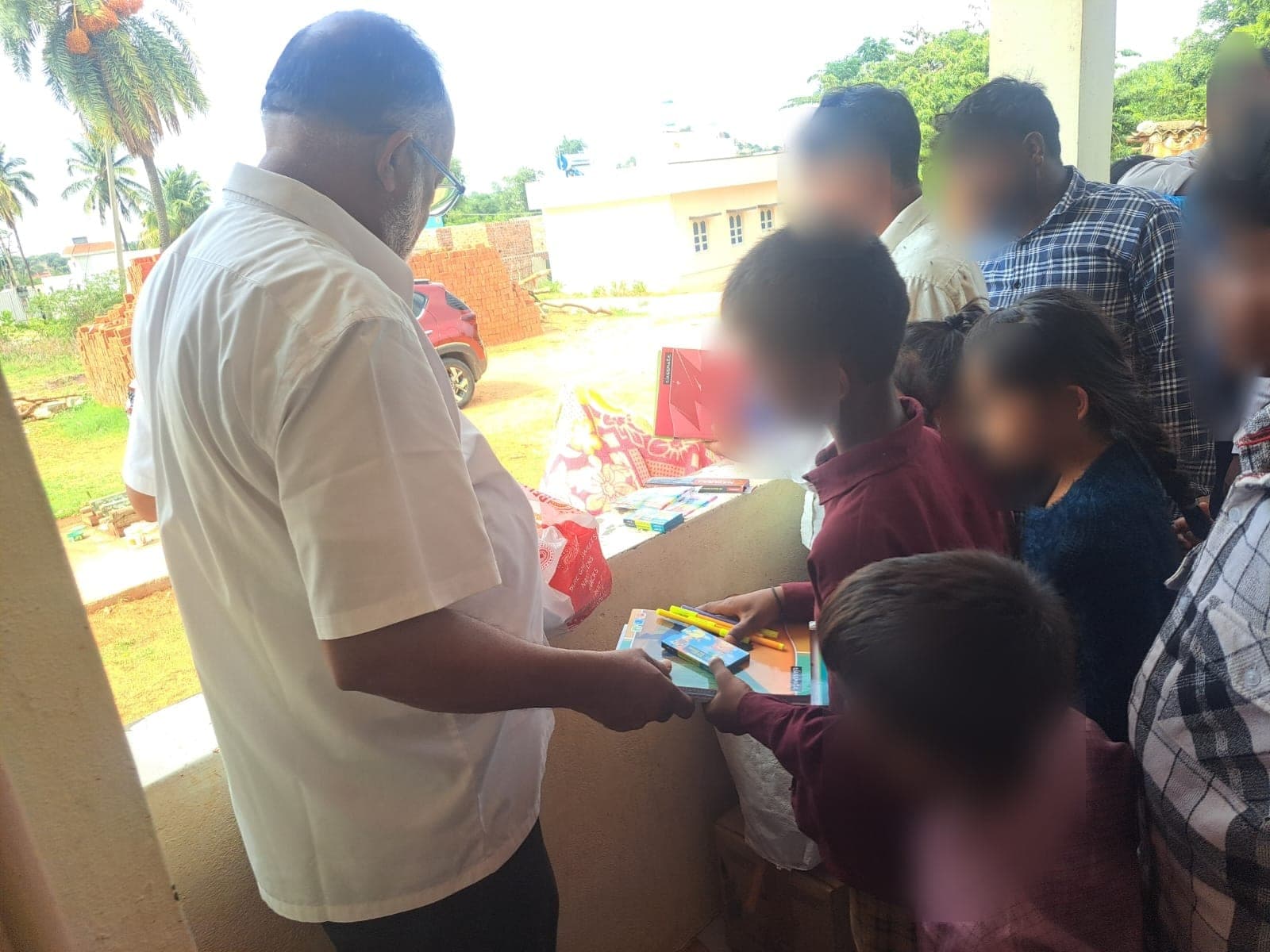 Children reaching for the remaining stationery sets at the end of a distribution. Faces are obscured to protect the children's privacy.